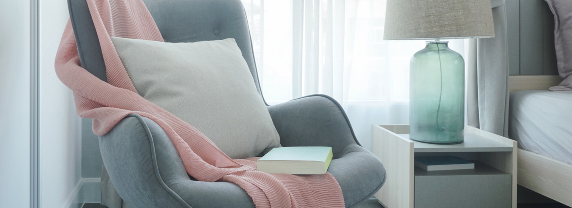 easy-armchair-with-pink-scarf-pillow-and-book-next-to-bed-in-the-bedroom